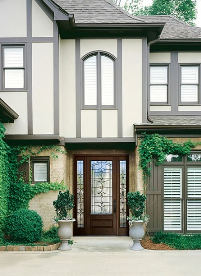 A Tudor-style house with symmetrical design, featuring a wooden door with glass panels, surrounded by climbing ivy and two planters, showcasing Alexander Company’s work in Burlingame.